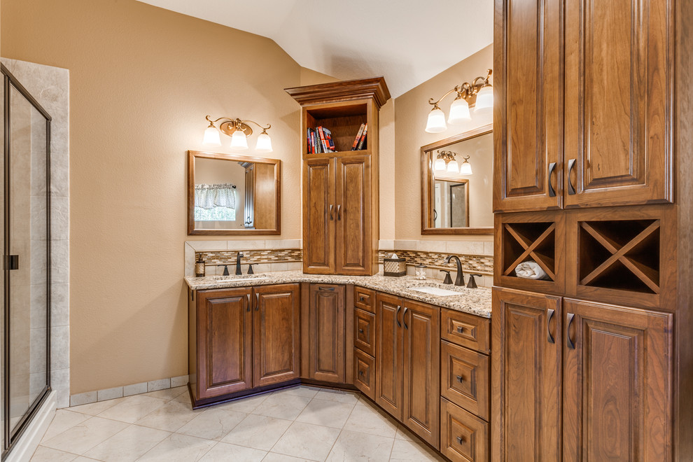 Photo of a mid-sized traditional master bathroom in Austin with beaded inset cabinets, brown cabinets, a corner tub, an alcove shower, a one-piece toilet, beige tile, ceramic tile, beige walls, ceramic floors, an integrated sink, granite benchtops, beige floor, a hinged shower door and beige benchtops.