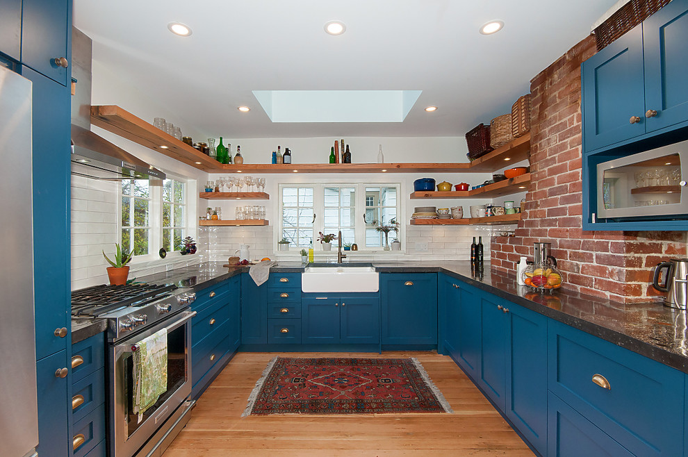 Photo of a country u-shaped kitchen in Vancouver with a farmhouse sink, shaker cabinets, blue cabinets, white splashback, subway tile splashback, stainless steel appliances, light hardwood floors, no island and beige floor.