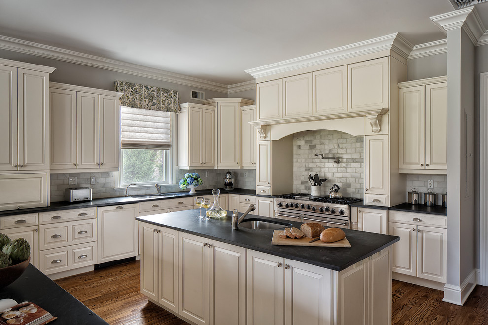 Open concept kitchen - large transitional medium tone wood floor and brown floor open concept kitchen idea with an undermount sink, raised-panel cabinets, white cabinets, solid surface countertops, gray backsplash, stone tile backsplash, stainless steel appliances and an island