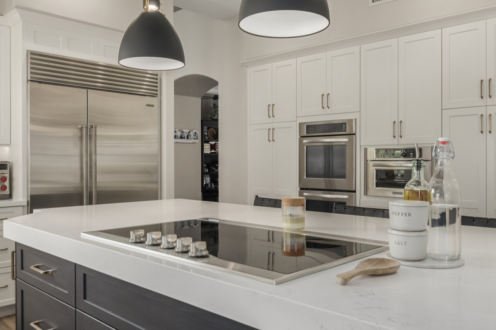 Mid-sized transitional u-shaped porcelain tile and brown floor enclosed kitchen photo in Phoenix with a farmhouse sink, shaker cabinets, white cabinets, quartz countertops, white backsplash, marble backsplash, stainless steel appliances, an island and white countertops