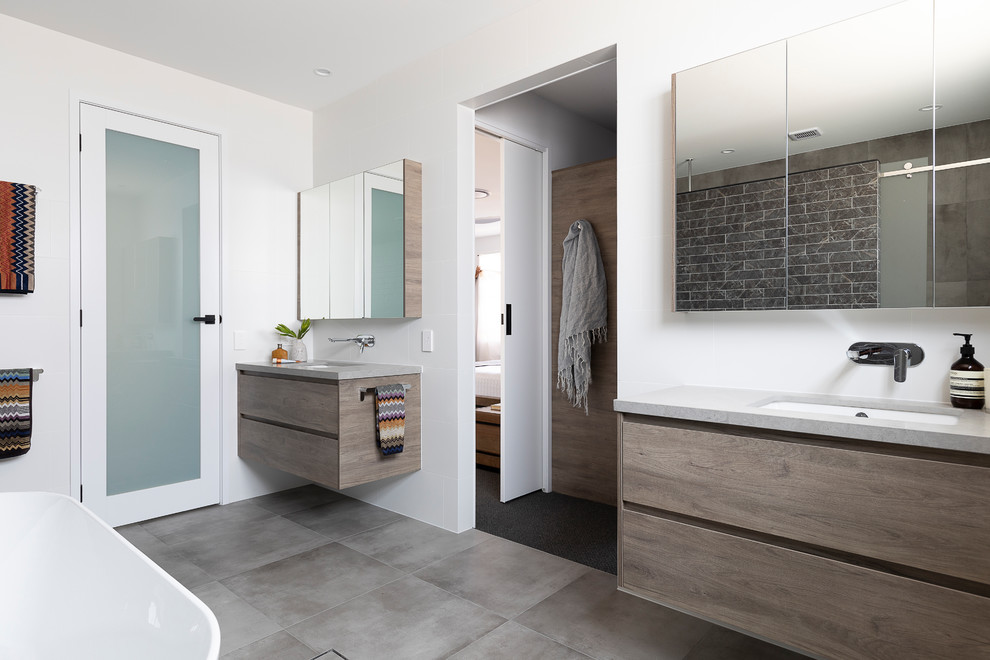 Large contemporary master bathroom in Brisbane with flat-panel cabinets, medium wood cabinets, a freestanding tub, a double shower, a one-piece toilet, white tile, ceramic tile, white walls, ceramic floors, an undermount sink, engineered quartz benchtops, grey floor, a sliding shower screen and grey benchtops.