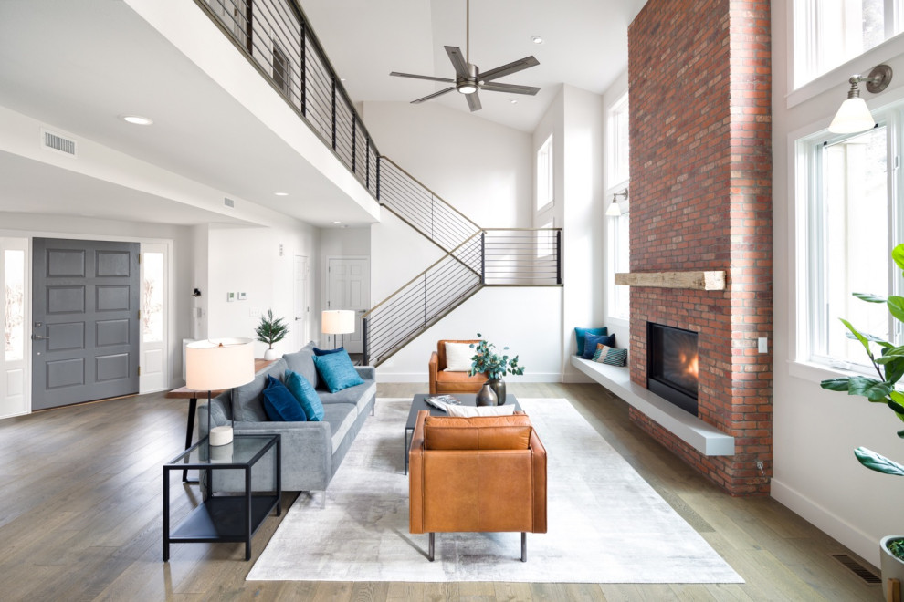 Large industrial open concept living room in Denver with white walls, medium hardwood floors, a standard fireplace, a brick fireplace surround, no tv and brown floor.