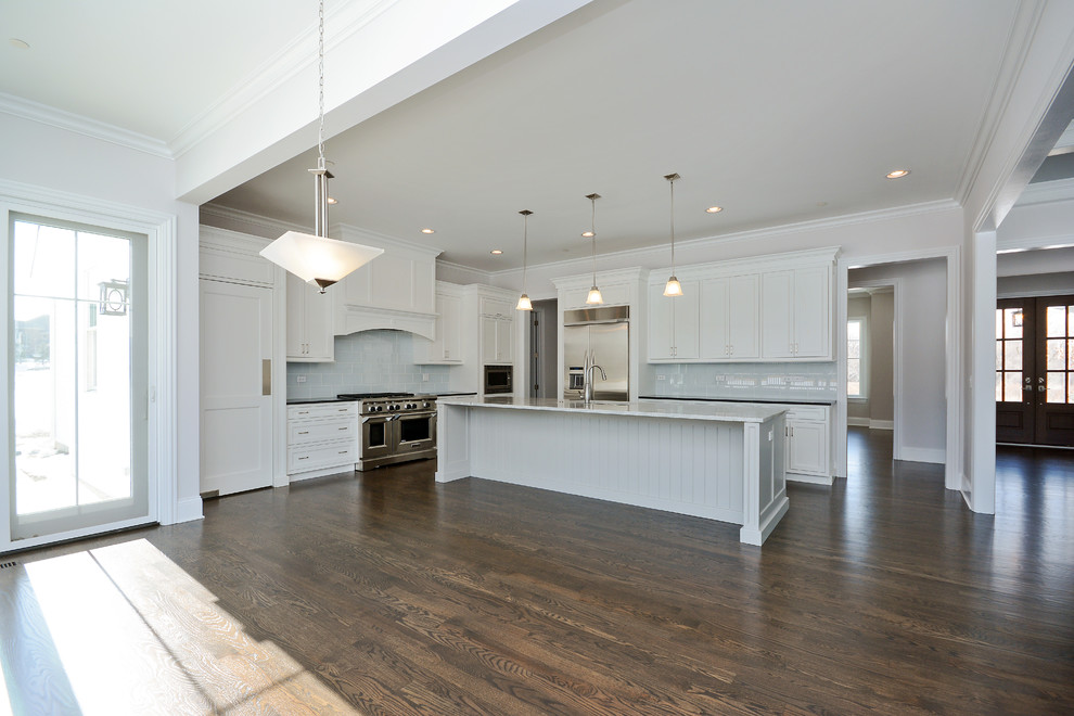 Photo of a large arts and crafts l-shaped eat-in kitchen in Chicago with an undermount sink, recessed-panel cabinets, white cabinets, granite benchtops, grey splashback, subway tile splashback, stainless steel appliances, medium hardwood floors and with island.
