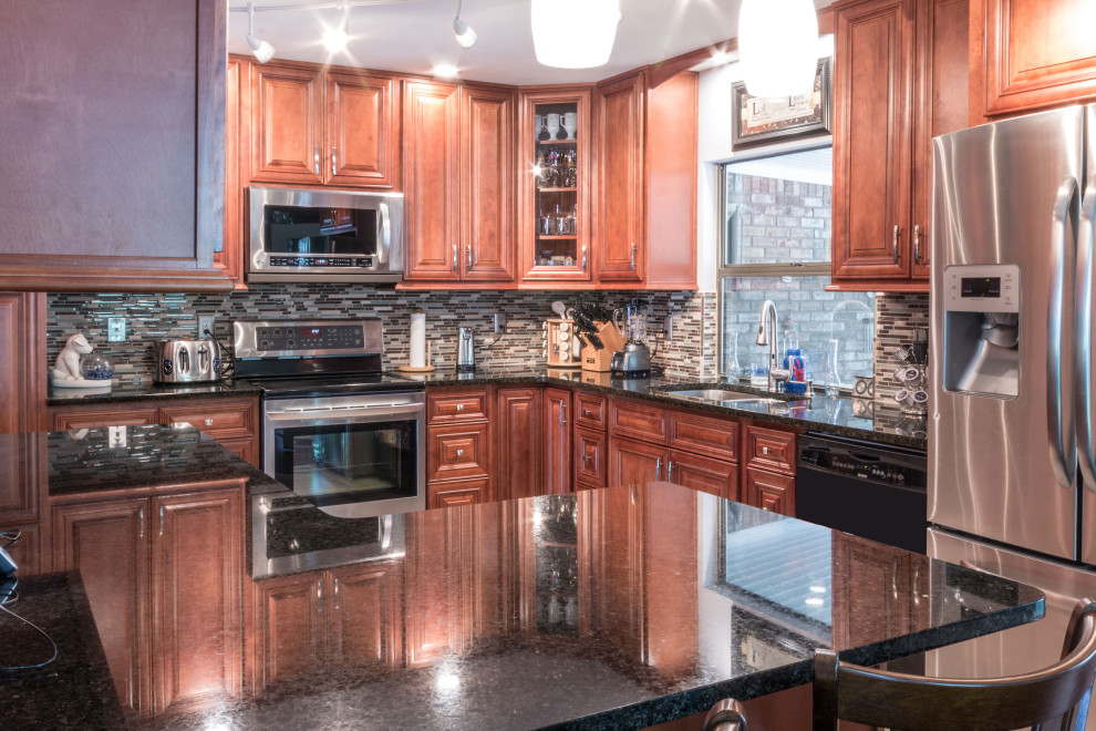 Kitchen - mid-sized l-shaped kitchen idea with an undermount sink, raised-panel cabinets, medium tone wood cabinets, granite countertops, glass tile backsplash, stainless steel appliances and black countertops