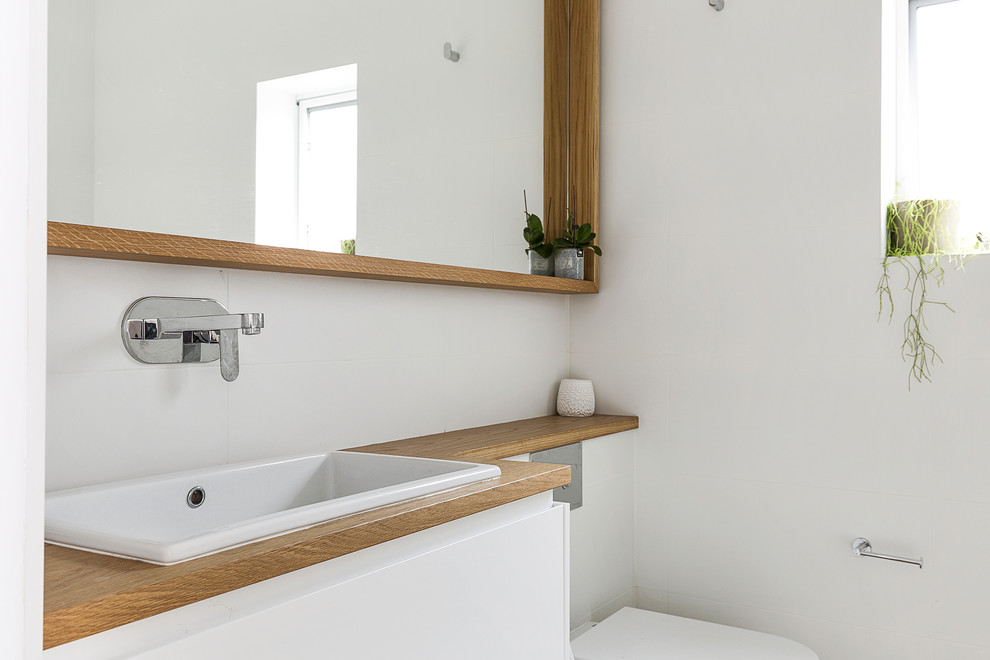 Inspiration for a mid-sized scandinavian master bathroom in Sydney with flat-panel cabinets, white cabinets, an open shower, a wall-mount toilet, white tile, ceramic tile, white walls, a drop-in sink, wood benchtops, porcelain floors, grey floor, an open shower and brown benchtops.
