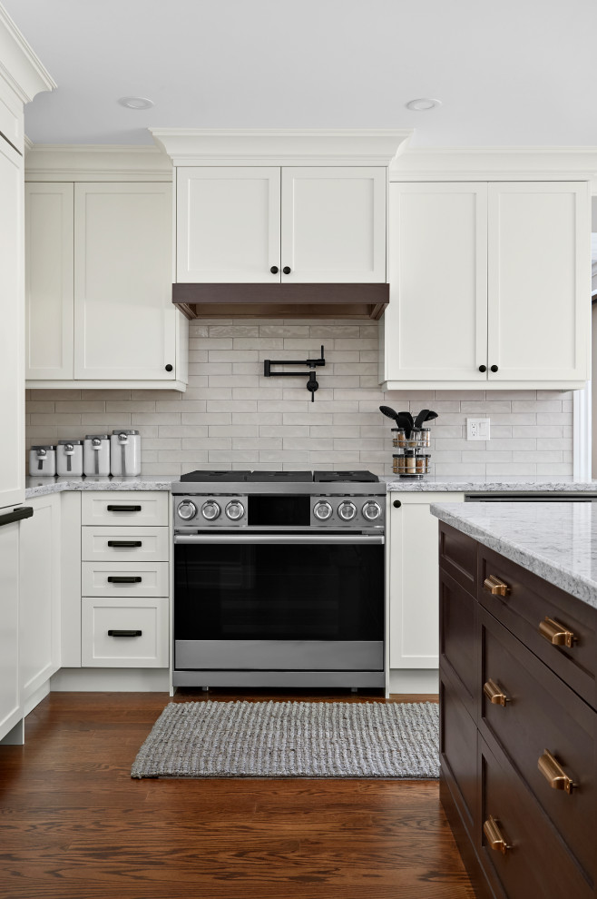Example of a transitional u-shaped medium tone wood floor and brown floor eat-in kitchen design in Toronto with shaker cabinets, white cabinets, quartz countertops, white backsplash, subway tile backsplash, stainless steel appliances, an island and gray countertops