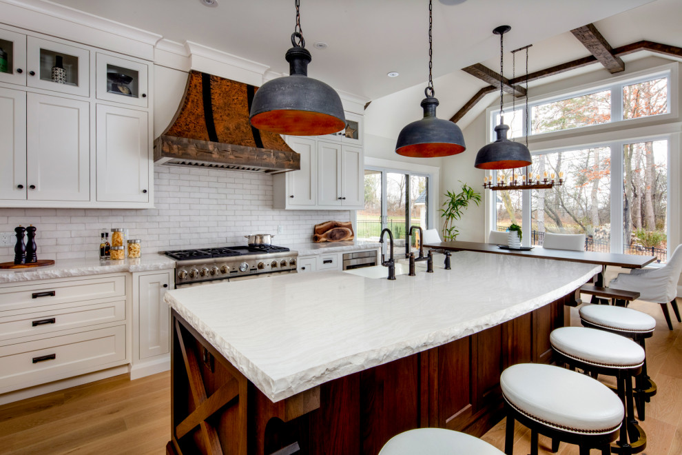 Design ideas for a large transitional eat-in kitchen in Toronto with a farmhouse sink, shaker cabinets, white cabinets, white splashback, subway tile splashback, stainless steel appliances, light hardwood floors, with island and white benchtop.