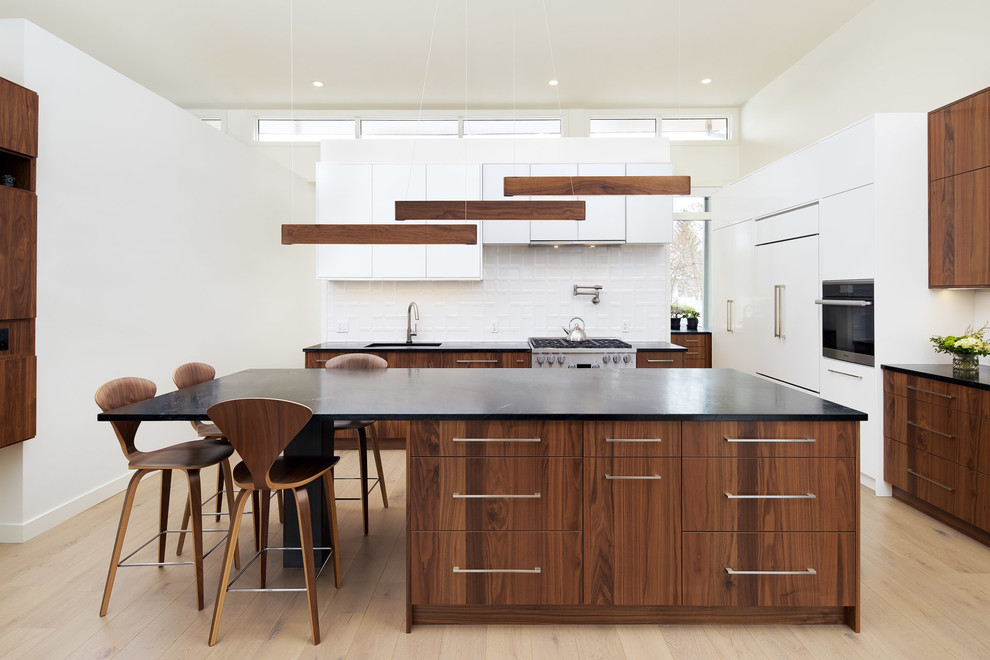 Example of a minimalist l-shaped light wood floor open concept kitchen design in Calgary with an undermount sink, flat-panel cabinets, dark wood cabinets, soapstone countertops, white backsplash, porcelain backsplash, stainless steel appliances, an island and black countertops