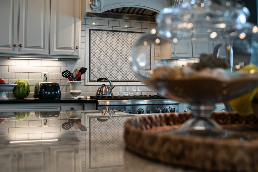 Large transitional l-shaped medium tone wood floor and brown floor open concept kitchen photo in Charlotte with a farmhouse sink, white cabinets, granite countertops, white backsplash, stainless steel appliances, an island, raised-panel cabinets, porcelain backsplash and white countertops
