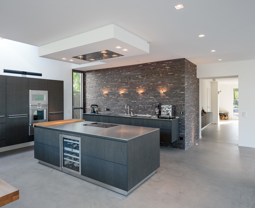 Large industrial l-shaped open plan kitchen in Cologne with a drop-in sink, flat-panel cabinets, dark wood cabinets, brown splashback, brick splashback, stainless steel appliances, vinyl floors, multiple islands and grey floor.