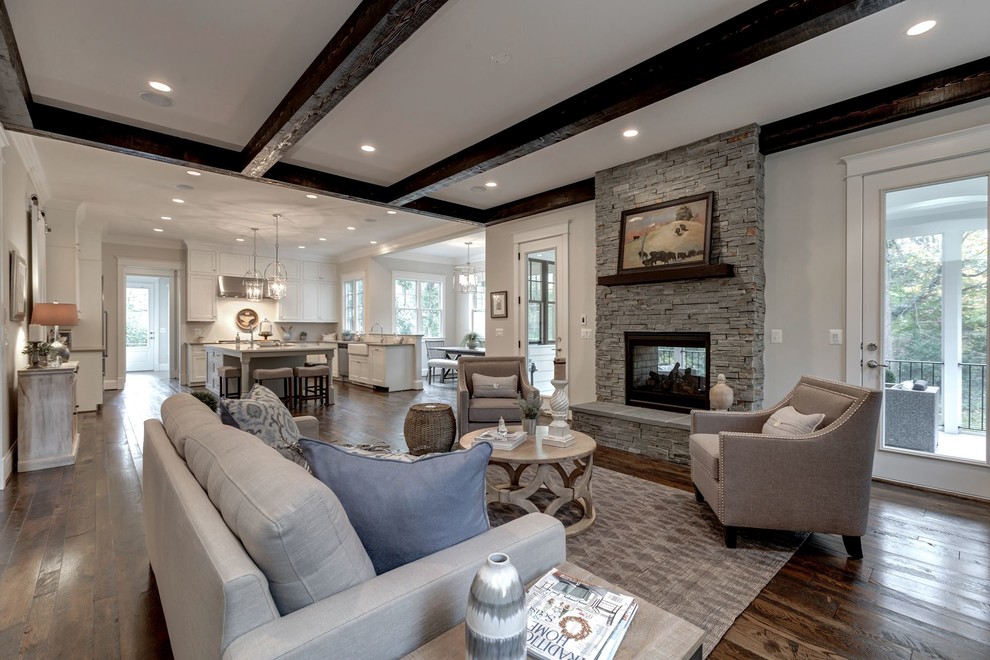 Large country open concept family room in DC Metro with beige walls, dark hardwood floors, a standard fireplace, a stone fireplace surround and a wall-mounted tv.