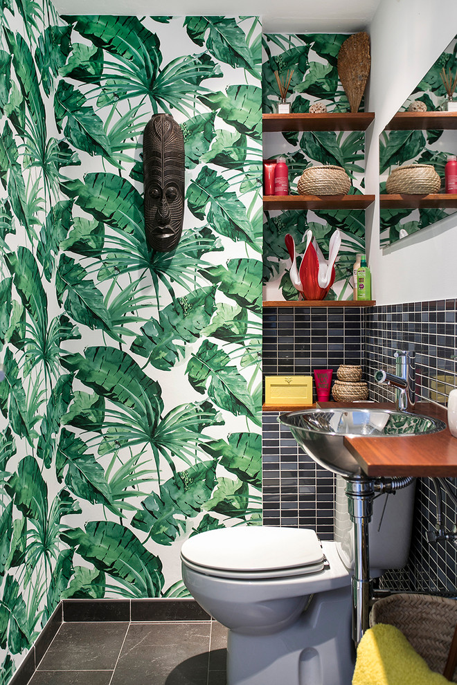 This is an example of a small tropical powder room in Barcelona with a two-piece toilet, multi-coloured walls, black tile, a drop-in sink and grey floor.