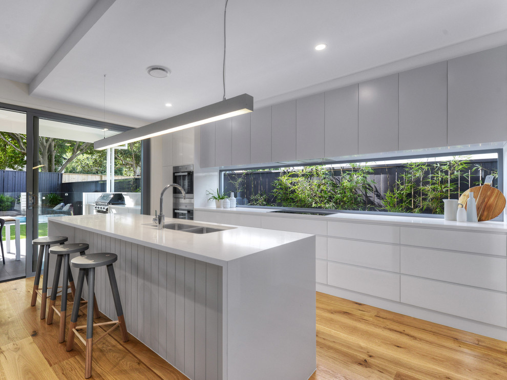 This is an example of a transitional galley open plan kitchen in Brisbane with an undermount sink, white cabinets, marble benchtops, window splashback, stainless steel appliances, medium hardwood floors and with island.