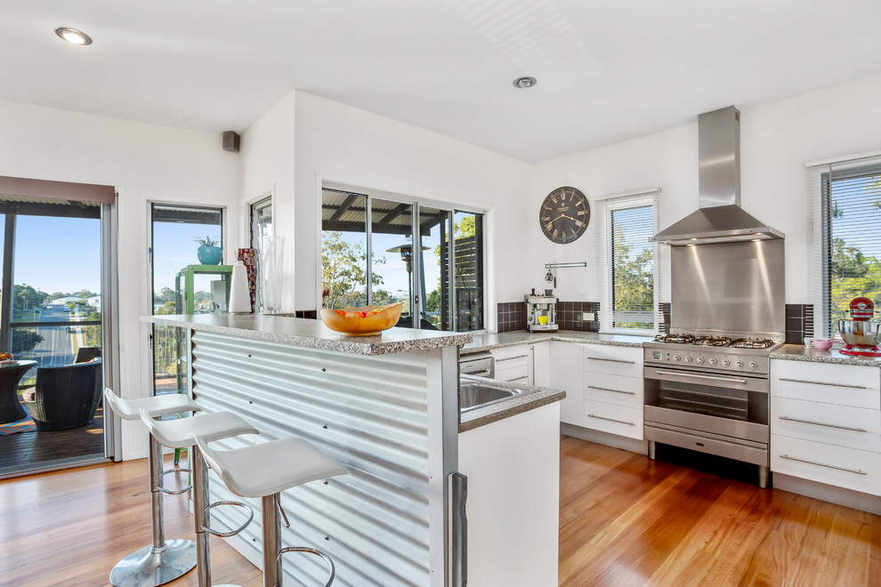 Mid-sized contemporary l-shaped kitchen in Gold Coast - Tweed with a drop-in sink, flat-panel cabinets, white cabinets, quartz benchtops, black splashback, ceramic splashback, stainless steel appliances, light hardwood floors and no island.