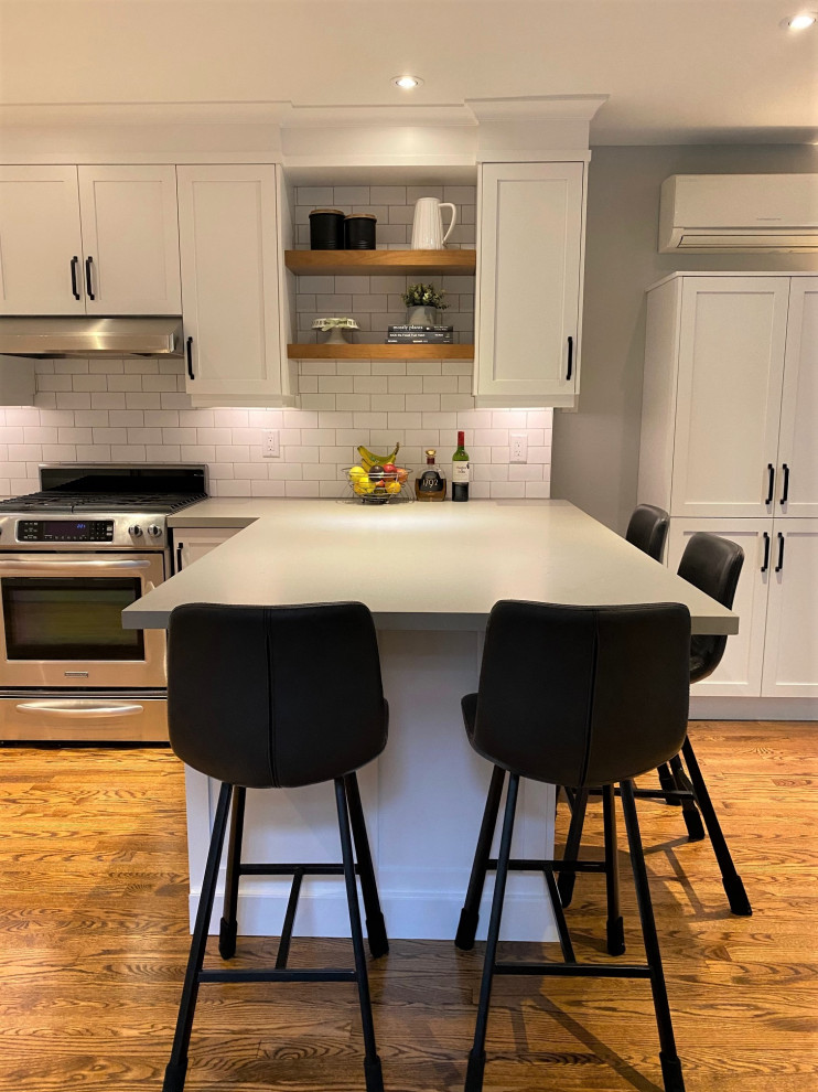 Inspiration for a mid-sized transitional u-shaped medium tone wood floor and brown floor open concept kitchen remodel in Toronto with an undermount sink, shaker cabinets, white cabinets, quartz countertops, white backsplash, porcelain backsplash, stainless steel appliances, a peninsula and gray countertops