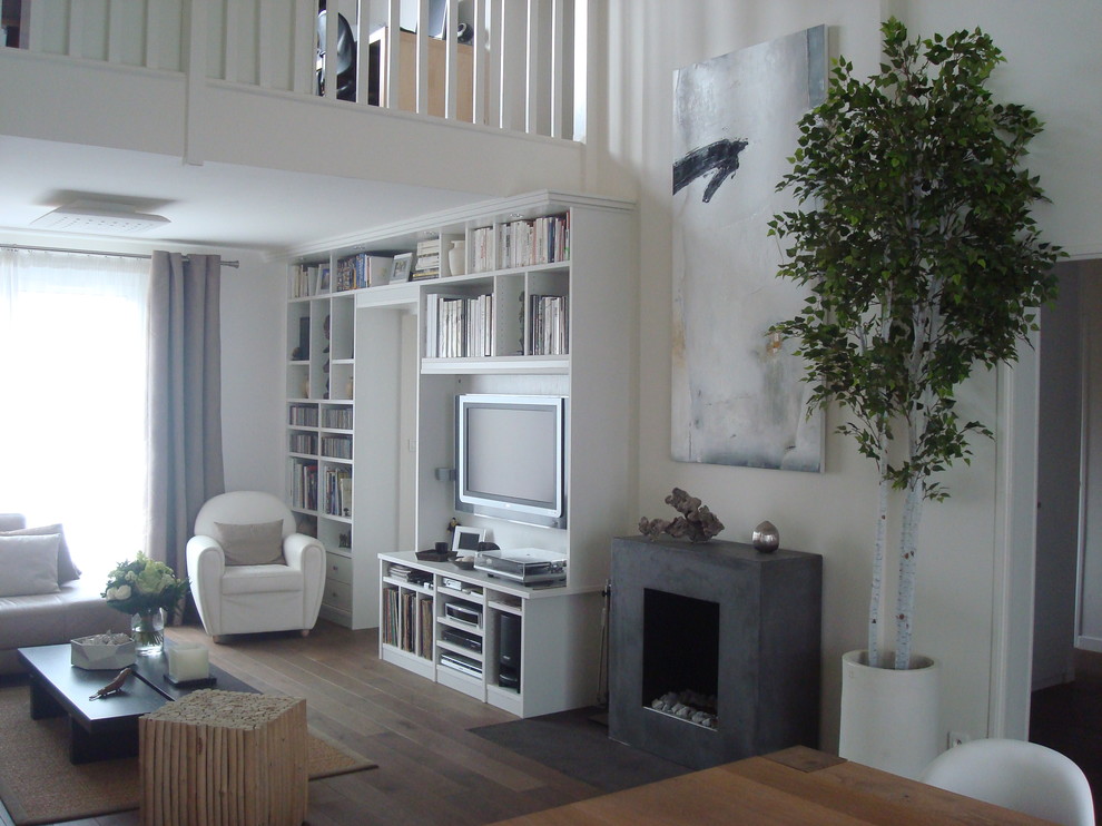 Photo of a mid-sized contemporary open concept living room in Paris with a library, white walls, medium hardwood floors, a standard fireplace and a wall-mounted tv.