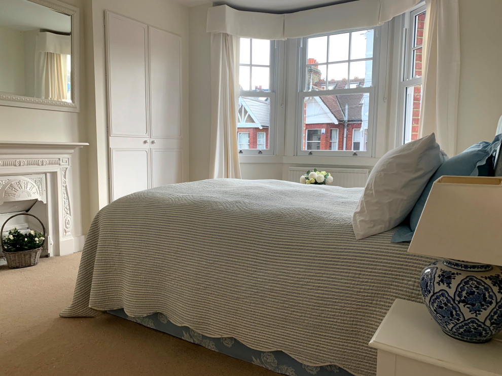 ロンドンにある広いトラディショナルスタイルのおしゃれな客用寝室 (白い壁、カーペット敷き、標準型暖炉、漆喰の暖炉まわり、ベージュの床)