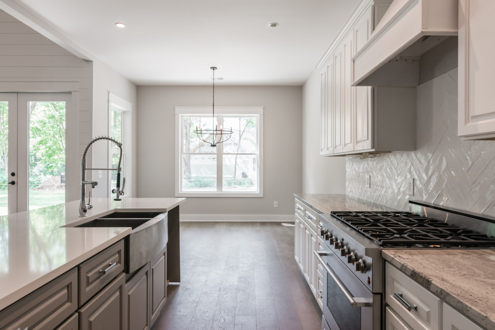 Large country l-shaped open plan kitchen in Nashville with a farmhouse sink, raised-panel cabinets, white cabinets, quartzite benchtops, grey splashback, ceramic splashback, stainless steel appliances, vinyl floors, with island, brown floor and grey benchtop.