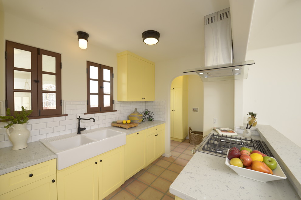Mid-sized mediterranean galley eat-in kitchen in Los Angeles with shaker cabinets, yellow cabinets, quartz benchtops, white splashback, subway tile splashback, panelled appliances, a farmhouse sink, terra-cotta floors and a peninsula.