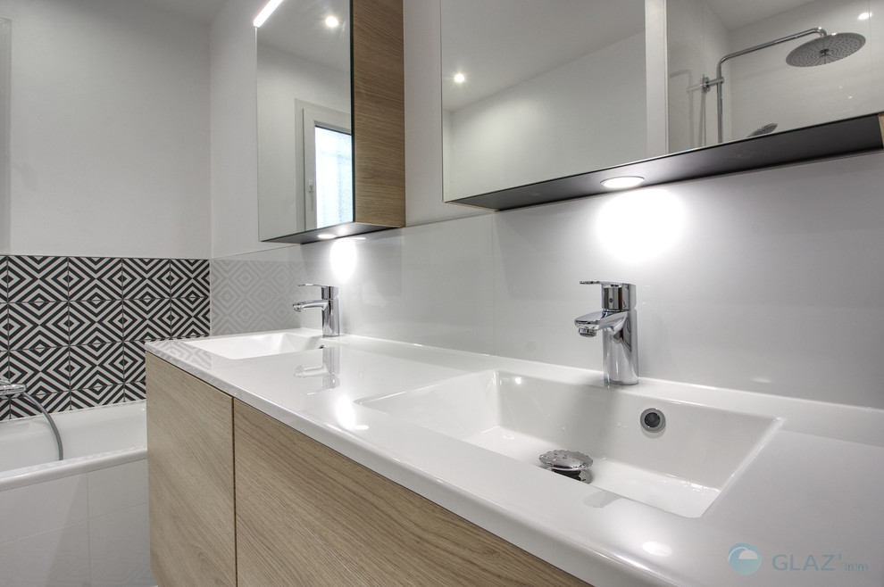 This is an example of a mid-sized contemporary master bathroom in Other with beaded inset cabinets, light wood cabinets, a drop-in tub, an alcove shower, a wall-mount toilet, white tile, ceramic tile, white walls, cement tiles, a drop-in sink, solid surface benchtops, black floor, a hinged shower door and white benchtops.