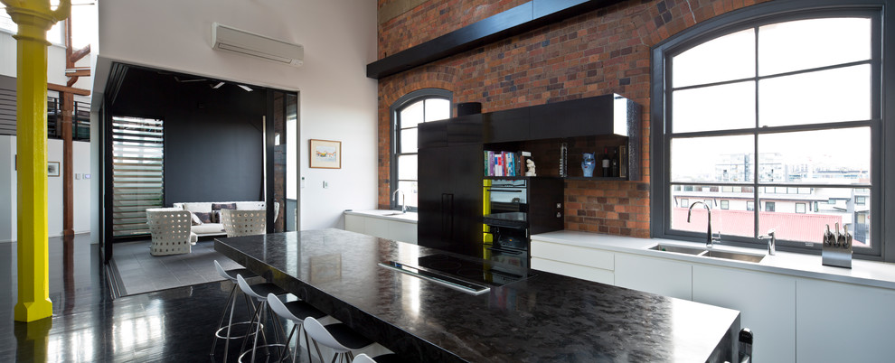 This is an example of a mid-sized industrial open plan kitchen in Brisbane with an undermount sink, flat-panel cabinets, white cabinets, marble benchtops, black appliances, dark hardwood floors, with island and black floor.