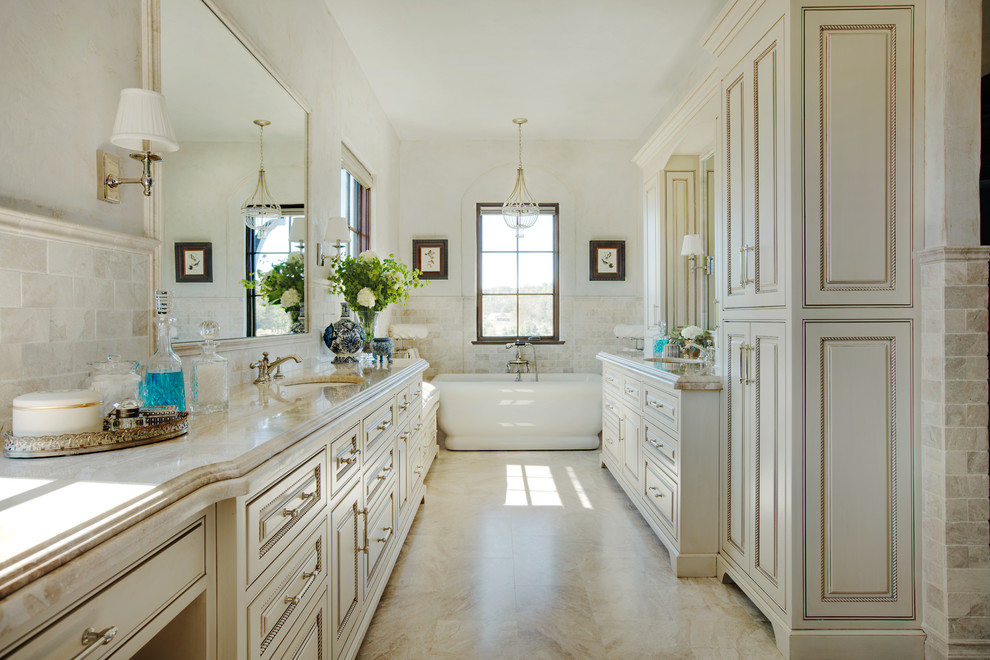 Mid-sized mediterranean master bathroom in Other with furniture-like cabinets, distressed cabinets, a freestanding tub, a curbless shower, a one-piece toilet, beige tile, subway tile, beige walls, limestone floors, an undermount sink and limestone benchtops.