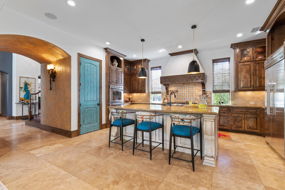 Mid-sized southwest u-shaped travertine floor and beige floor eat-in kitchen photo in Houston with a farmhouse sink, raised-panel cabinets, brown cabinets, granite countertops, beige backsplash, travertine backsplash, stainless steel appliances, an island and orange countertops