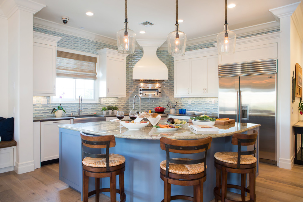 This is an example of a traditional l-shaped kitchen in Los Angeles with a farmhouse sink, shaker cabinets, white cabinets, blue splashback, stainless steel appliances, light hardwood floors, with island and beige floor.
