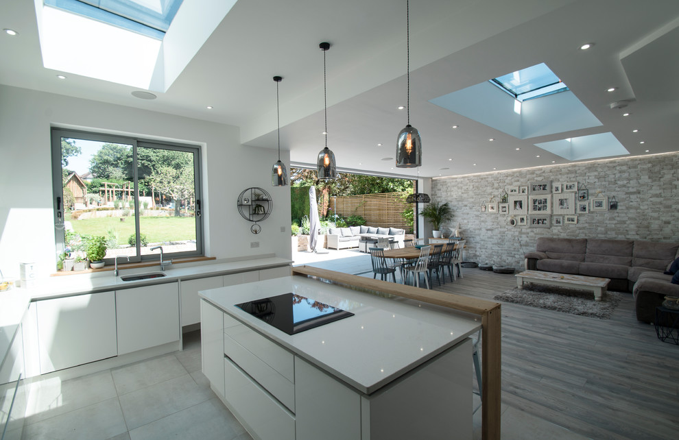 Photo of a large contemporary l-shaped open plan kitchen in Surrey with a drop-in sink, flat-panel cabinets, white cabinets, solid surface benchtops, grey splashback, glass sheet splashback, stainless steel appliances, vinyl floors, with island, grey floor and white benchtop.