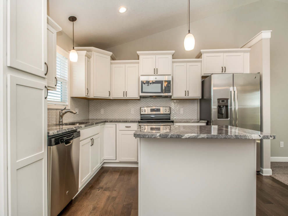 Large transitional medium tone wood floor and brown floor eat-in kitchen photo with an undermount sink, shaker cabinets, white cabinets, granite countertops, white backsplash, subway tile backsplash, stainless steel appliances, an island and multicolored countertops