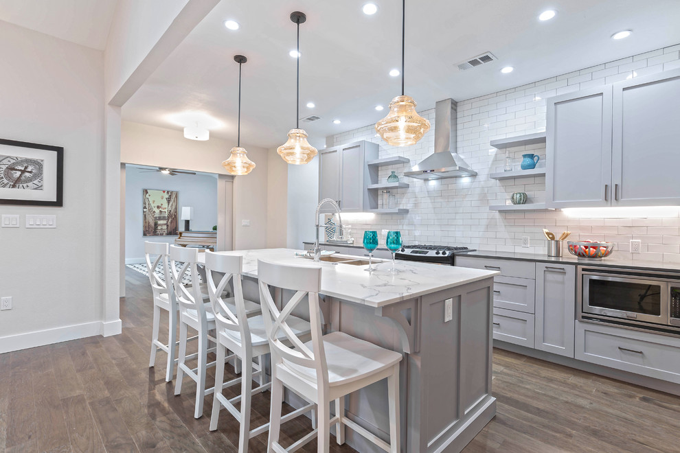 Inspiration for a mid-sized transitional galley medium tone wood floor open concept kitchen remodel in Dallas with a double-bowl sink, shaker cabinets, gray cabinets, quartz countertops, white backsplash, subway tile backsplash, stainless steel appliances and an island
