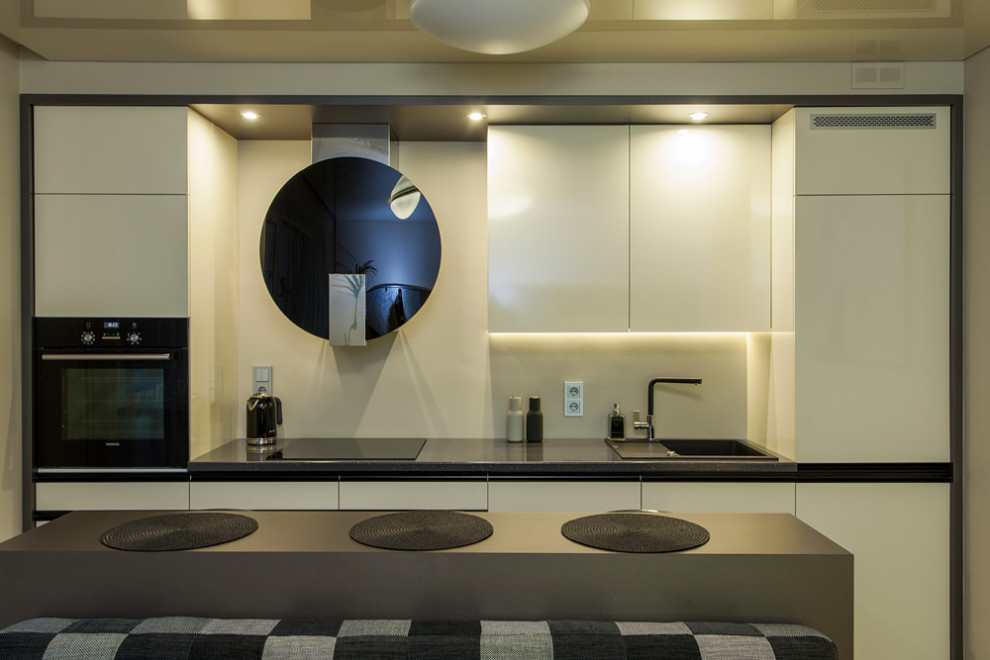 Immagine di una cucina contemporanea di medie dimensioni con lavello da incasso, ante beige, top in laminato, elettrodomestici neri e pavimento in legno massello medio