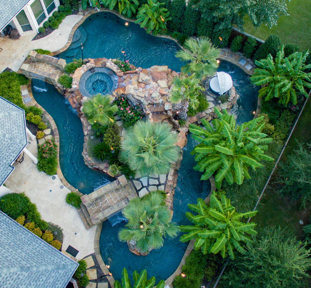 This is an example of a large tropical backyard custom-shaped pool in Dallas with a water feature and natural stone pavers.