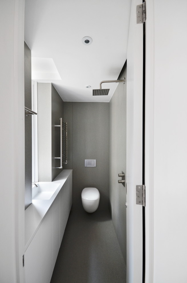 This is an example of a small contemporary master wet room bathroom in London with flat-panel cabinets, white cabinets, a wall-mount toilet, gray tile, porcelain tile, grey walls, porcelain floors, a console sink, solid surface benchtops, grey floor, an open shower and white benchtops.