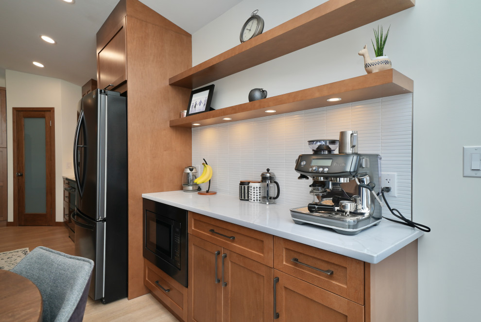 L-shaped vinyl floor and beige floor eat-in kitchen photo with a single-bowl sink, shaker cabinets, brown cabinets, quartz countertops, white backsplash, ceramic backsplash, black appliances, an island and white countertops