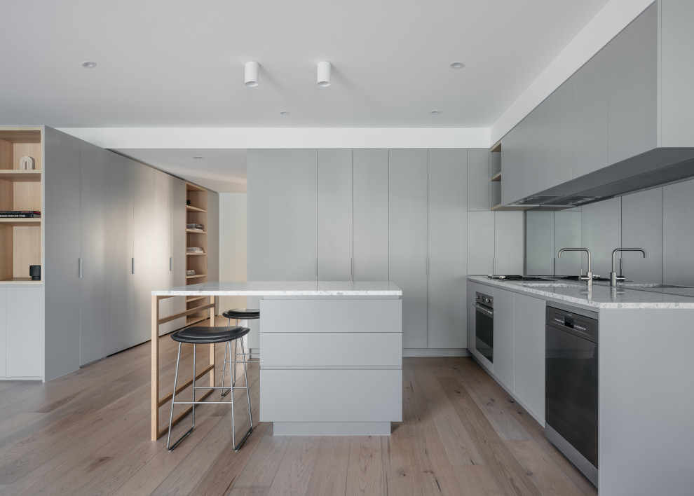 Design ideas for a modern l-shaped kitchen in Melbourne with an undermount sink, flat-panel cabinets, grey cabinets, stainless steel appliances, light hardwood floors, with island, beige floor and grey benchtop.