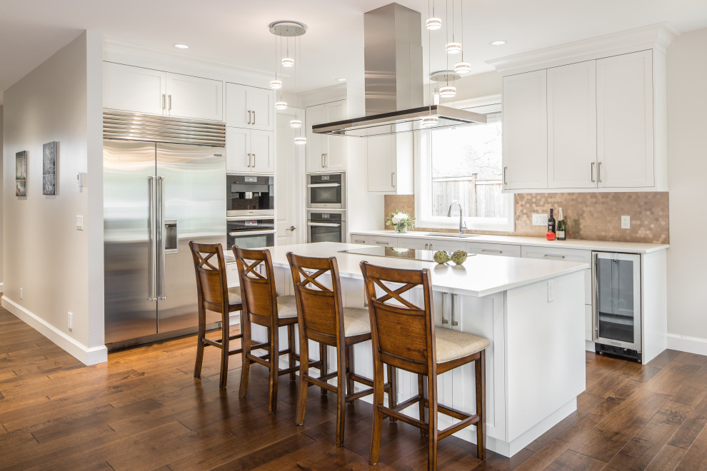 Inspiration for a transitional l-shaped dark wood floor and brown floor kitchen remodel in Vancouver with an undermount sink, shaker cabinets, white cabinets, beige backsplash, mosaic tile backsplash, stainless steel appliances, an island and white countertops