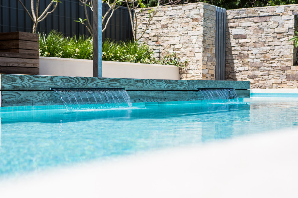 This is an example of a large contemporary backyard rectangular aboveground pool in Perth with a water feature and natural stone pavers.