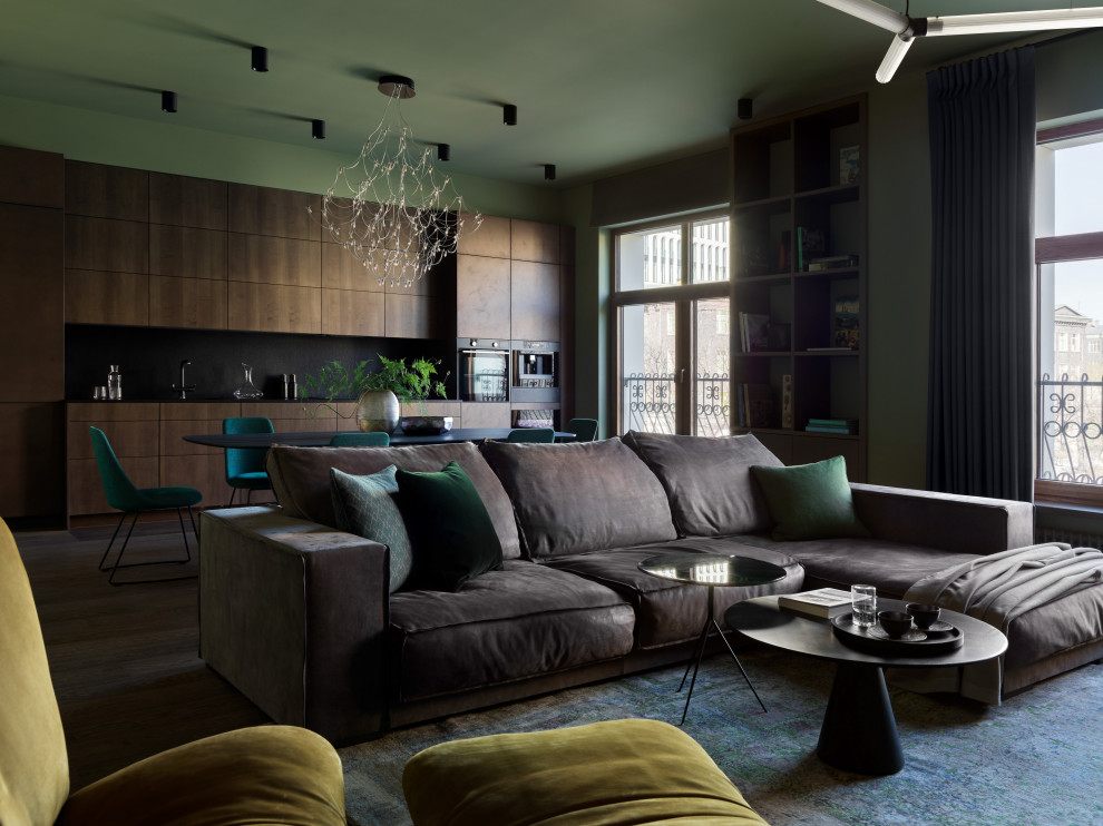 На фото: большая открытая гостиная комната в современном стиле с зелеными стенами, темным паркетным полом, телевизором на стене и коричневым полом с