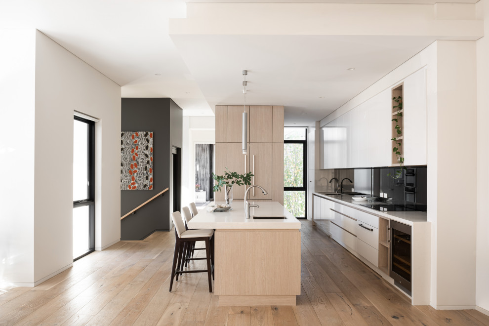 This is an example of a contemporary galley kitchen in Perth with an undermount sink, flat-panel cabinets, white cabinets, black splashback, panelled appliances, medium hardwood floors, with island, brown floor and white benchtop.