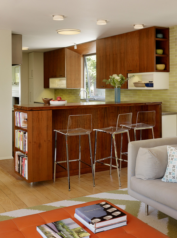 This is an example of a midcentury galley open plan kitchen in San Francisco with flat-panel cabinets, medium wood cabinets, green splashback, light hardwood floors and brown benchtop.