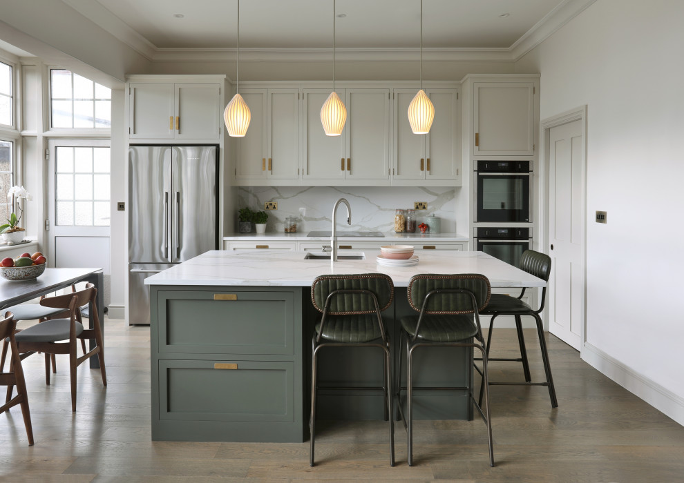 Inspiration for a mid-sized transitional single-wall open plan kitchen in London with a single-bowl sink, shaker cabinets, grey cabinets, quartzite benchtops, engineered quartz splashback, stainless steel appliances, medium hardwood floors, with island and white benchtop.