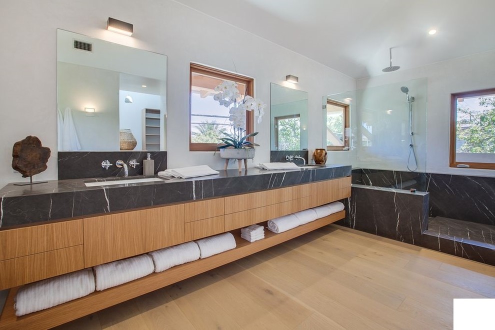 Large asian master bathroom in Los Angeles with flat-panel cabinets, light wood cabinets, an open shower, white tile, white walls, light hardwood floors, an undermount sink, marble benchtops, brown floor, an open shower and black benchtops.