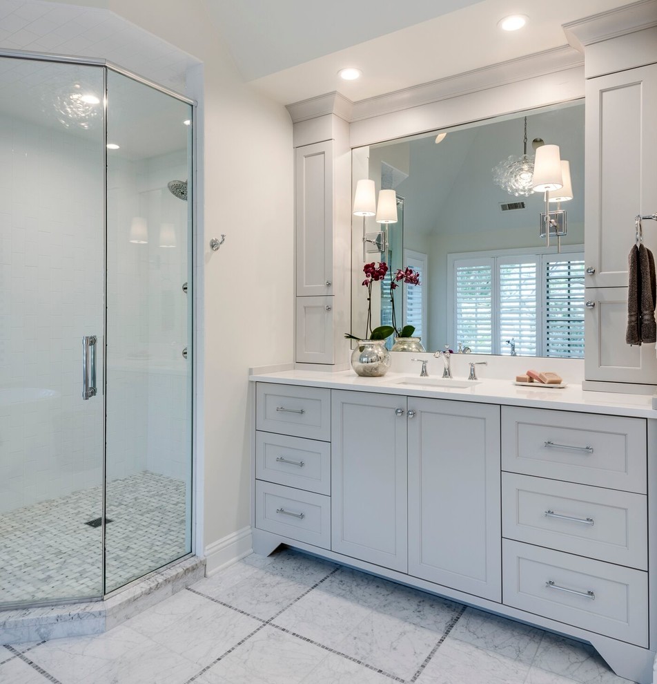 This is an example of a large transitional master bathroom in Chicago with recessed-panel cabinets, white cabinets, a freestanding tub, a corner shower, white tile, stone slab, white walls, marble floors, an undermount sink and solid surface benchtops.