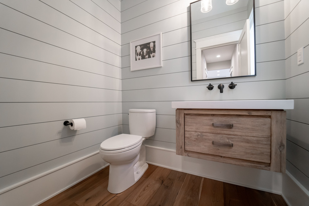 This is an example of a transitional bathroom in Chicago with medium wood cabinets, a two-piece toilet, grey walls, medium hardwood floors, brown floor, white benchtops and flat-panel cabinets.