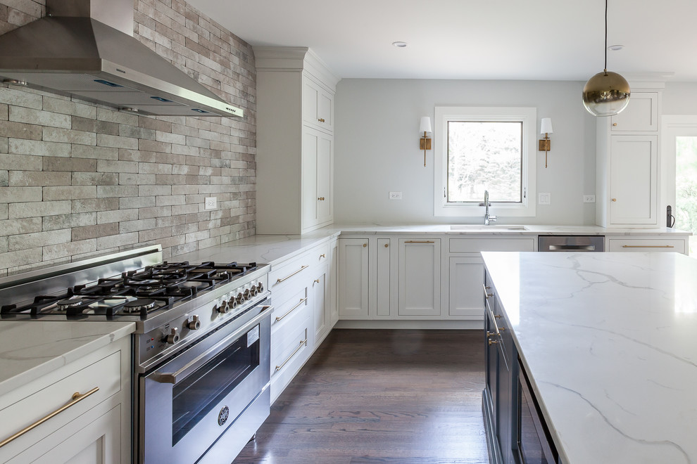 This is an example of a large transitional u-shaped open plan kitchen in Chicago with an undermount sink, shaker cabinets, white cabinets, quartz benchtops, brown splashback, ceramic splashback, stainless steel appliances, medium hardwood floors, with island and brown floor.