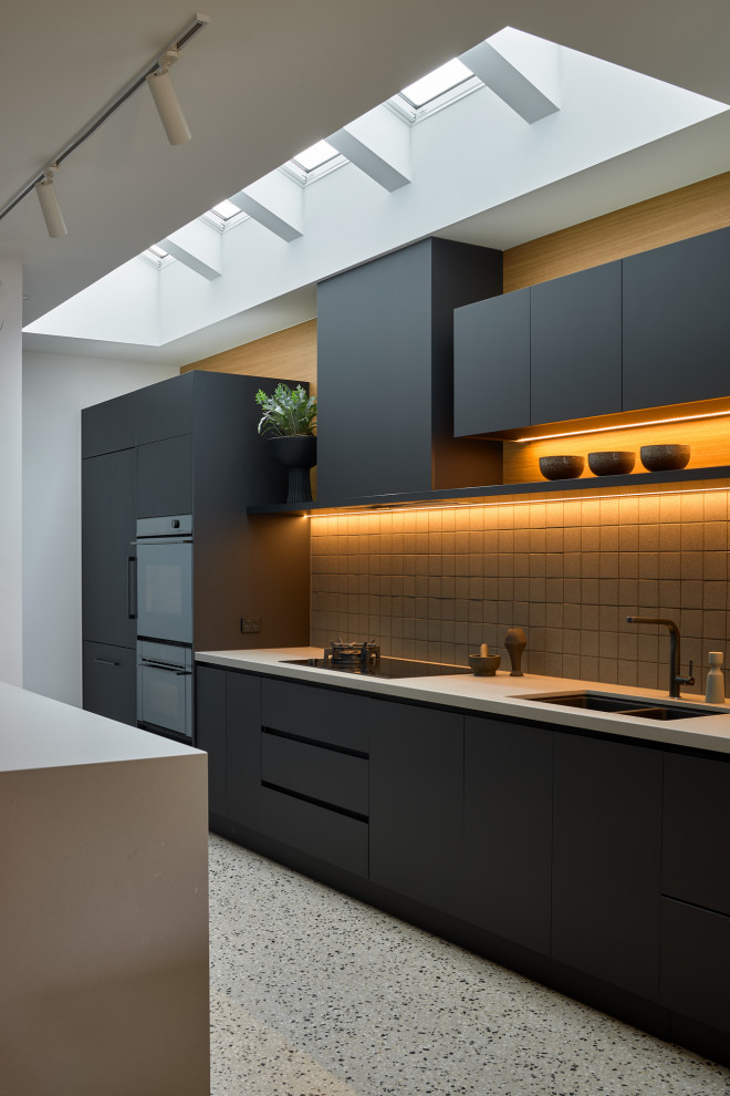 Design ideas for a large contemporary kitchen in Melbourne with flat-panel cabinets, black cabinets, solid surface benchtops, grey splashback, mosaic tile splashback, black appliances, concrete floors, with island, multi-coloured floor and grey benchtop.