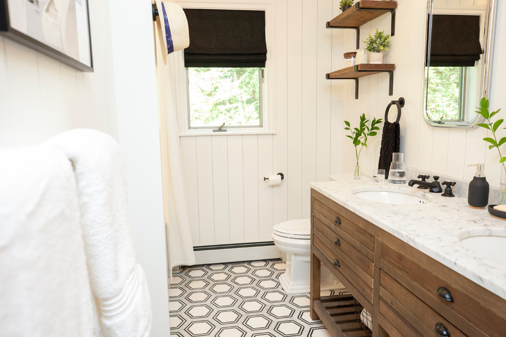 This is an example of a mid-sized country kids bathroom in New York with distressed cabinets, an alcove tub, a shower/bathtub combo, a two-piece toilet, ceramic tile, white walls, marble floors, an undermount sink, marble benchtops, black floor and a shower curtain.