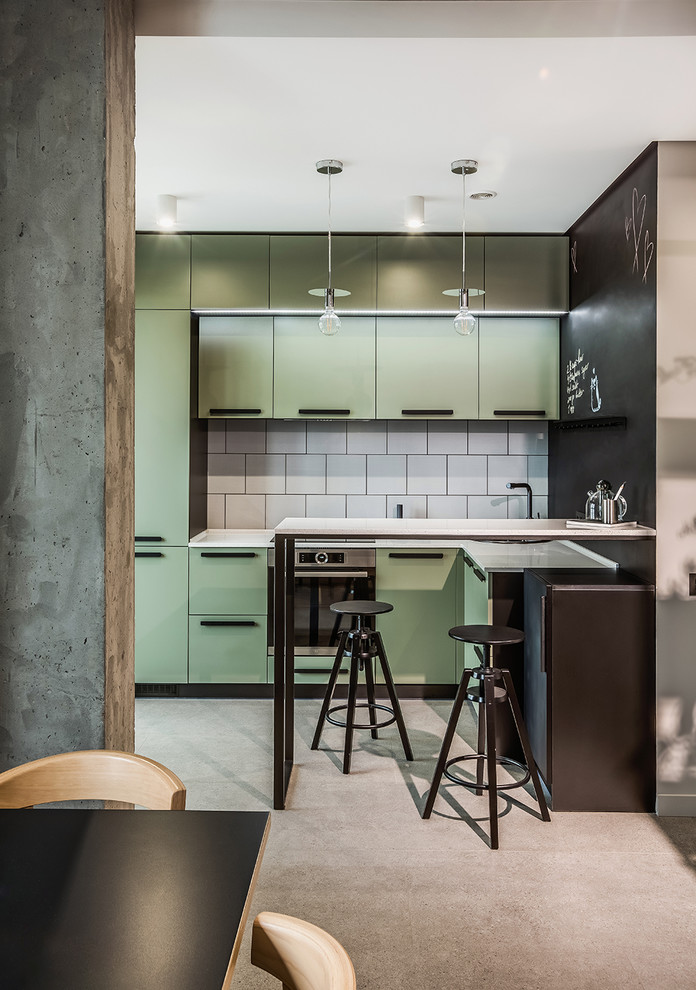This is an example of a small contemporary galley eat-in kitchen in Other with green cabinets, concrete floors, flat-panel cabinets, white splashback, stainless steel appliances, a peninsula, grey floor and white benchtop.
