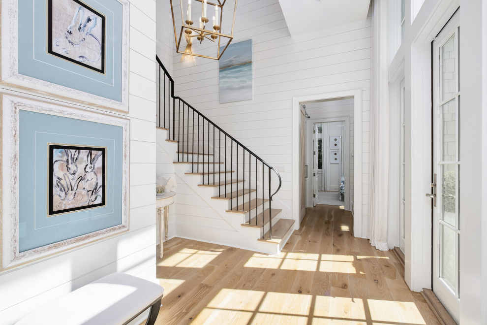 Immagine di un grande ingresso costiero con pareti bianche, pavimento in legno massello medio, una porta singola, una porta bianca, pavimento marrone e pareti in perlinato